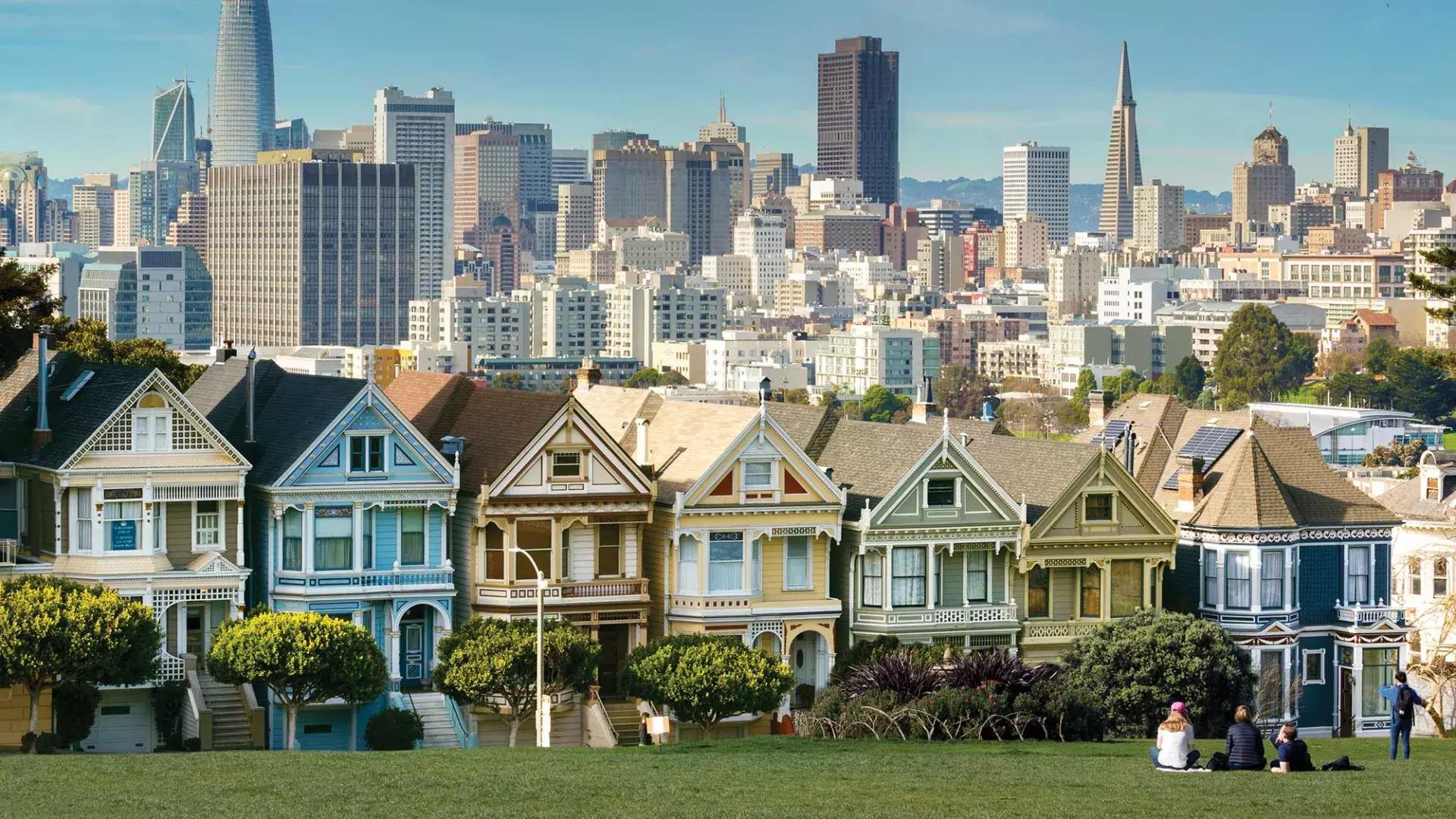 Picnickers sit on the grass at Alamo Square Park with the Painted Ladies and San Francisco skyline in the background.